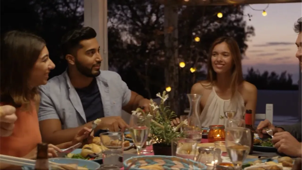 Frame from the Freshly ad: the host laughing at a dusk dinner table under string lights, dishes spread